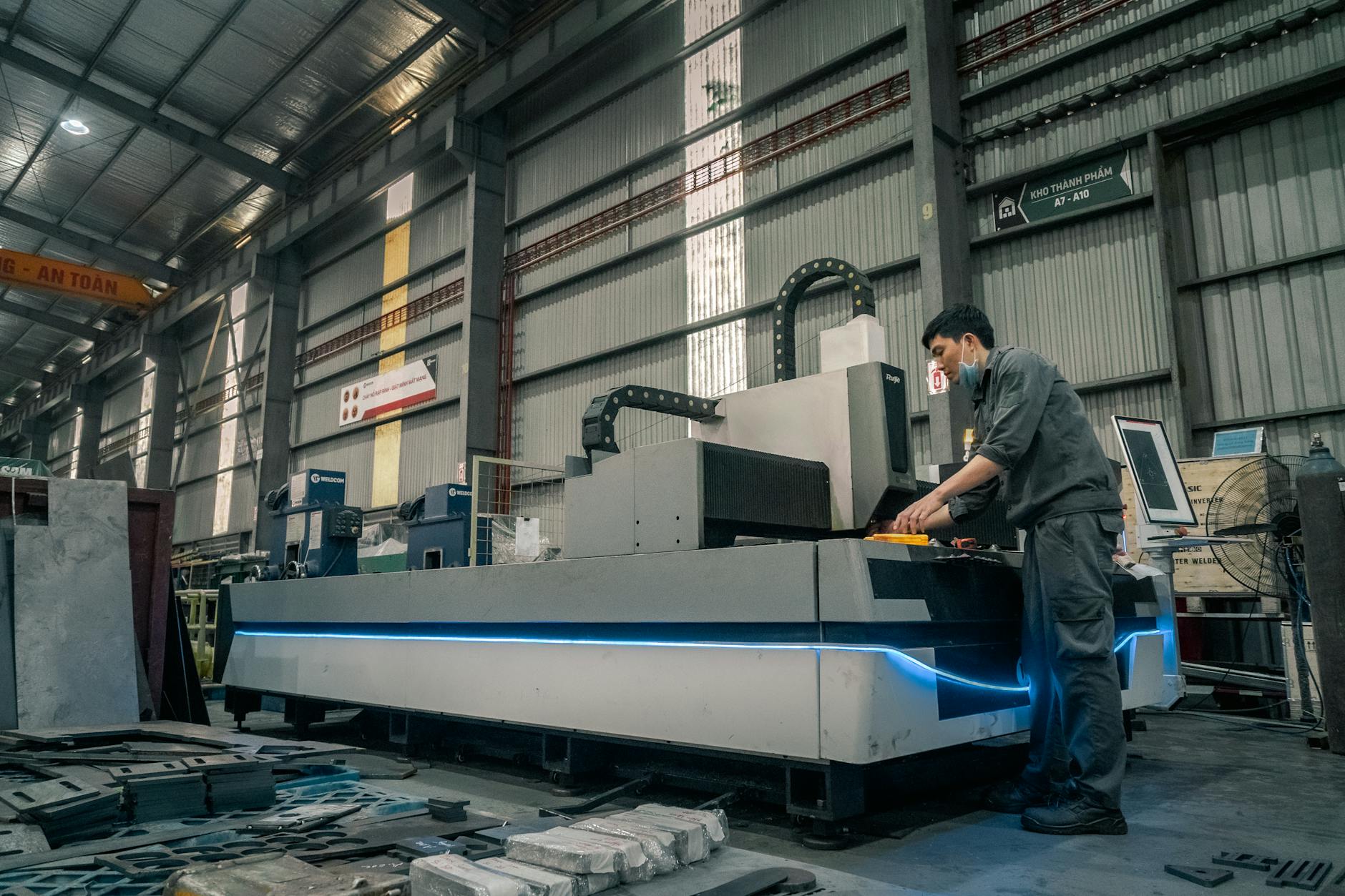 Pracownik w maseczce obsługujący maszynę w dużej hali produkcyjnej