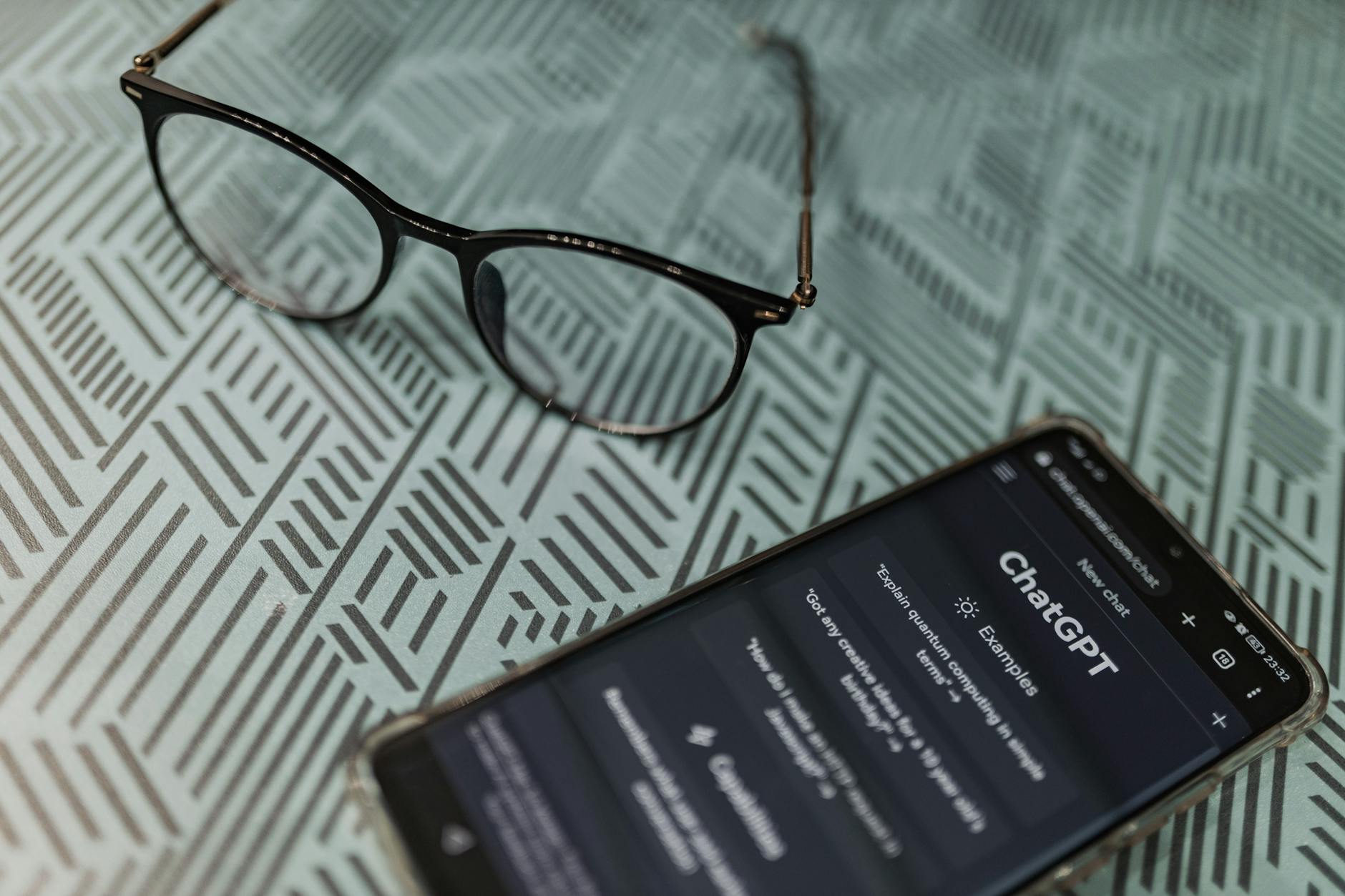Okulary obok smartfona z aplikacją ChatGPT na wzorzystym tle
